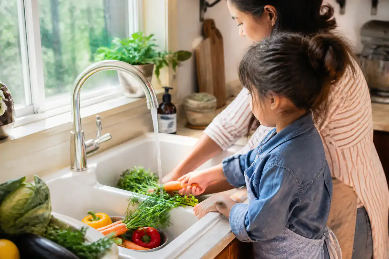 A child and parent washing vegetables together at a kitchen counter